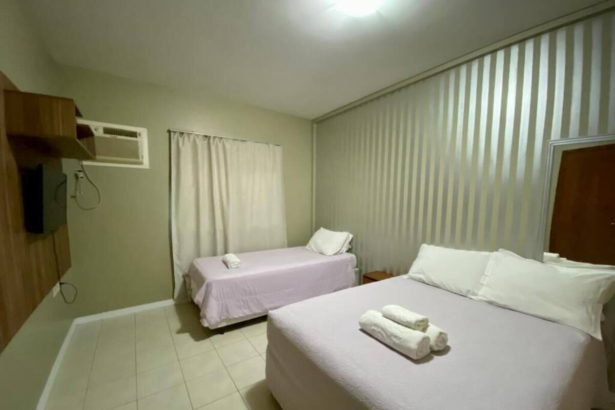 A hotel room with two beds, a TV, a window with blinds, and a tiled floor.