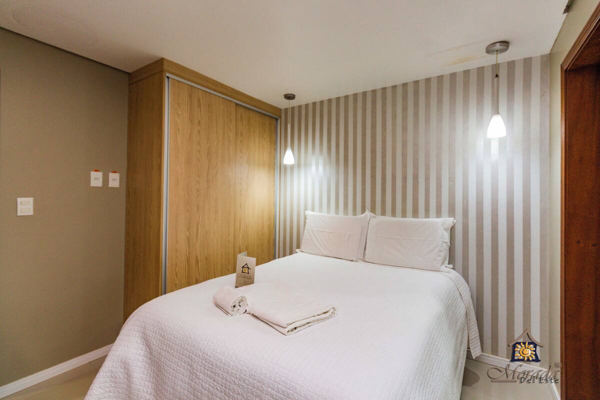 A hotel room with a bed, wooden wardrobe, and striped wallpaper.