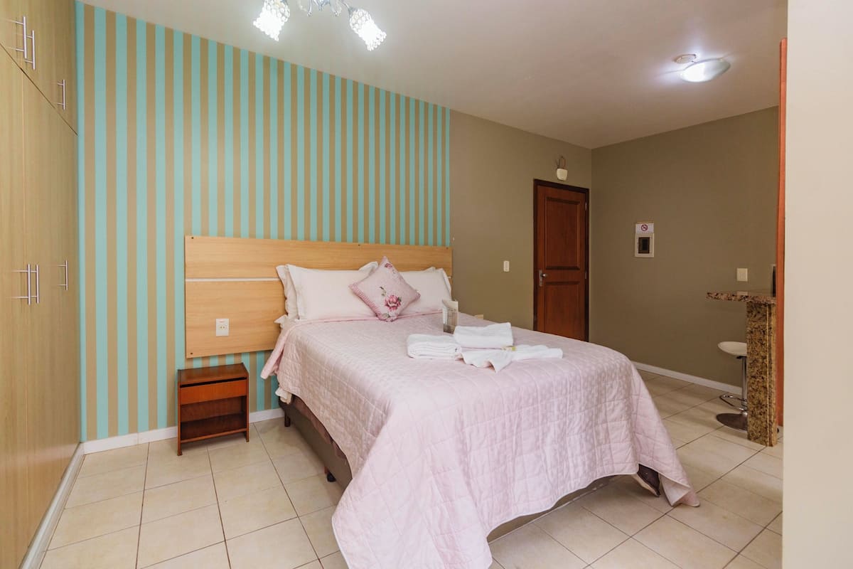 A bedroom with a bed, a nightstand, a wardrobe, a door, and a small bathroom area.