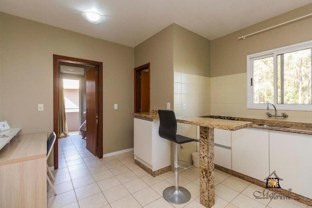 A kitchen with a granite countertop, a black bar stool, and a window with a view of trees.