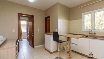 A kitchen with a granite countertop, a black bar stool, and a window with a view of trees.