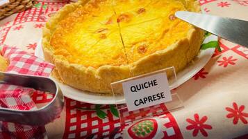 Una quiche sobre un plato blanco con una etiqueta, colocada sobre una mesa con mantel a cuadros rojo y blanco.