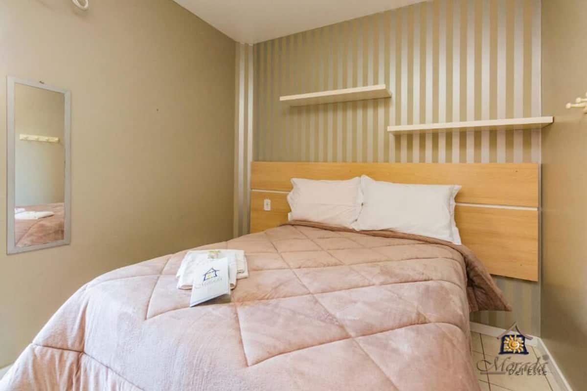 A neatly made bed with a wooden headboard, a bedside table with a lamp, and a striped wall.
