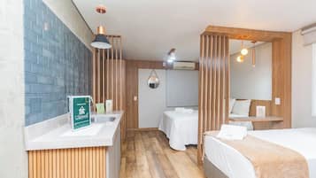 Habitación de hotel con suelo de madera, dos camas, un baño con espejo y un lavabo con un letrero verde.