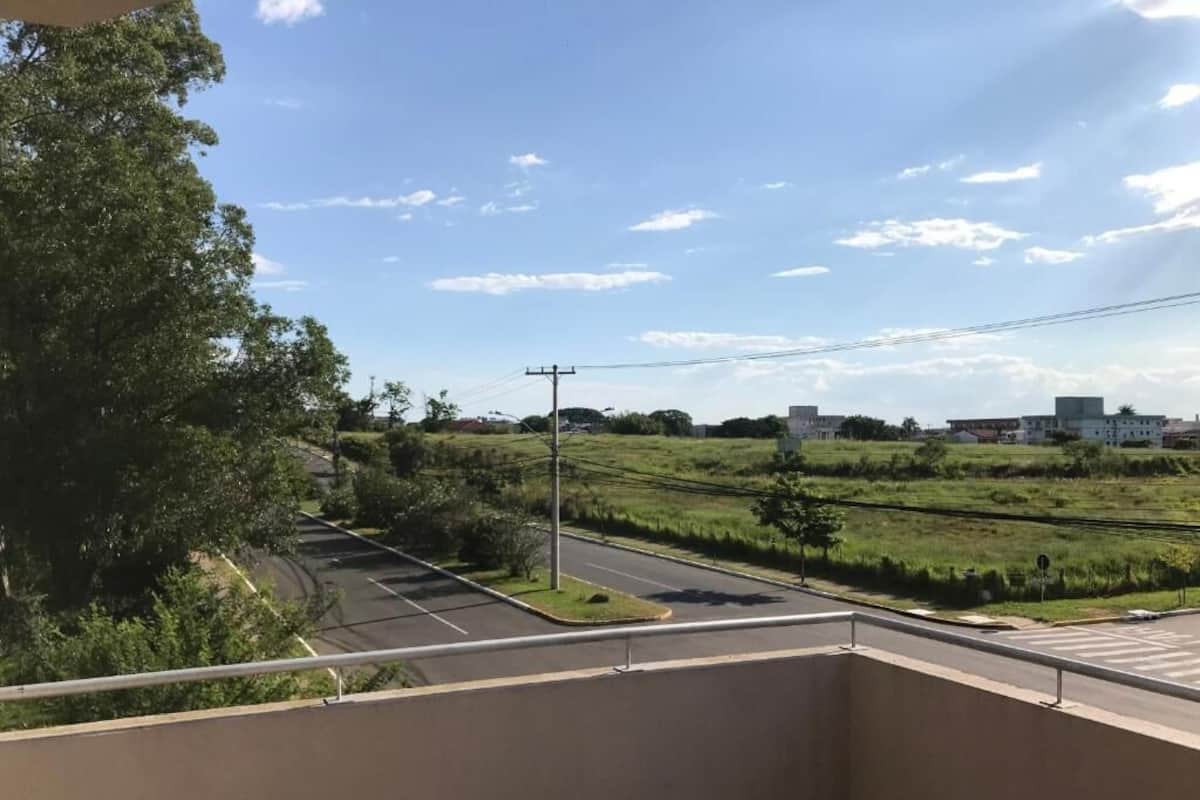 A balcony with a view of a parking lot and a green field.