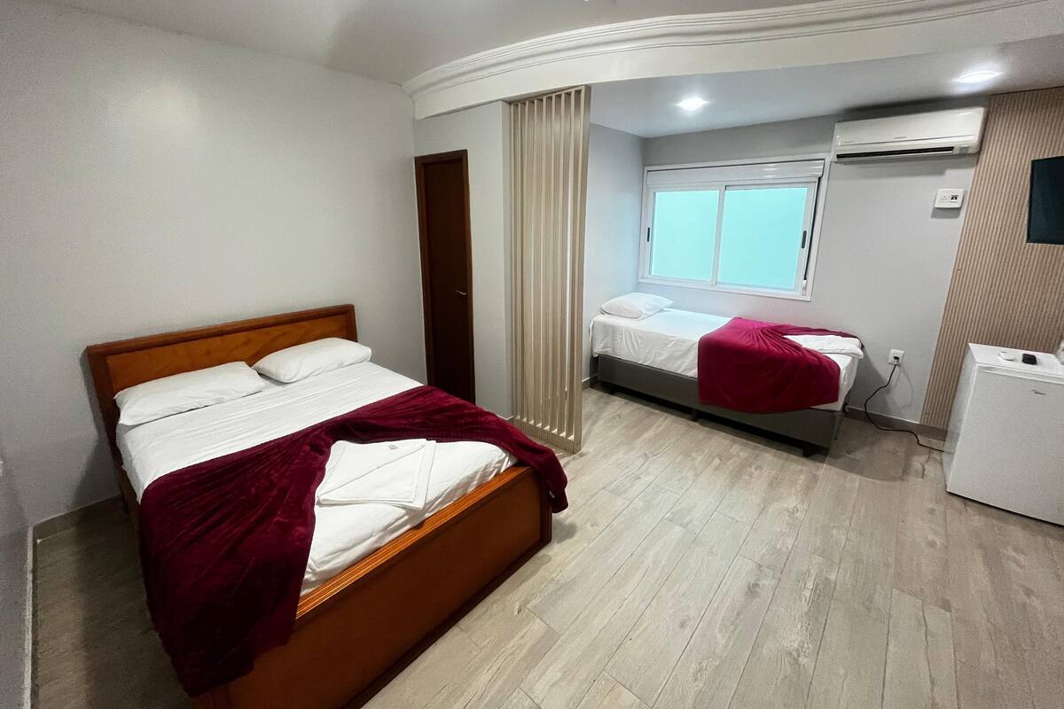 A hotel room with a large bed, a smaller bed, a desk, and an air conditioning unit.