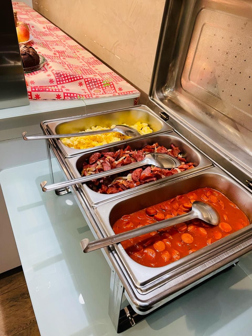 A buffet with various food options including scrambled eggs, sausages, and a tomato-based dish.