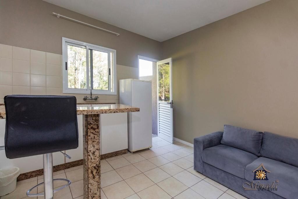A compact kitchen with a dining area, a grey sofa, and a window providing natural light.