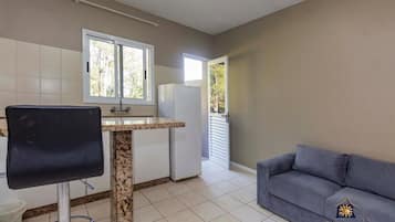 A compact kitchen with a dining area, a grey sofa, and a window providing natural light.