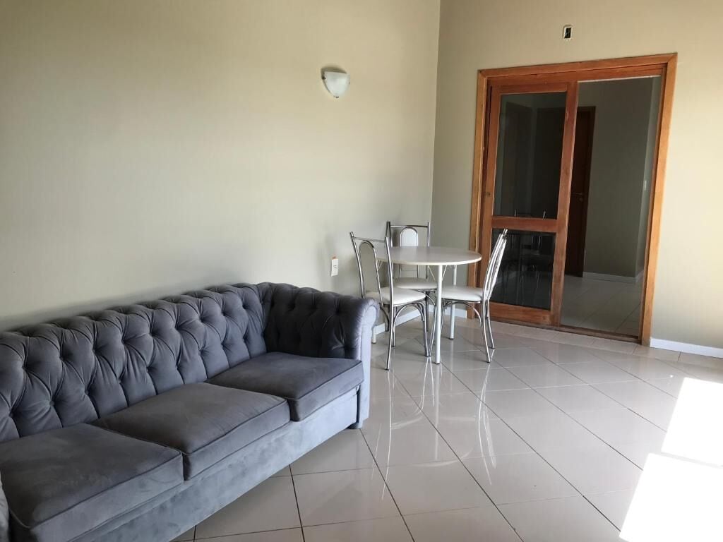 Una sala de estar con un sofá gris, una mesa de comedor con sillas y una puerta corrediza de vidrio.
