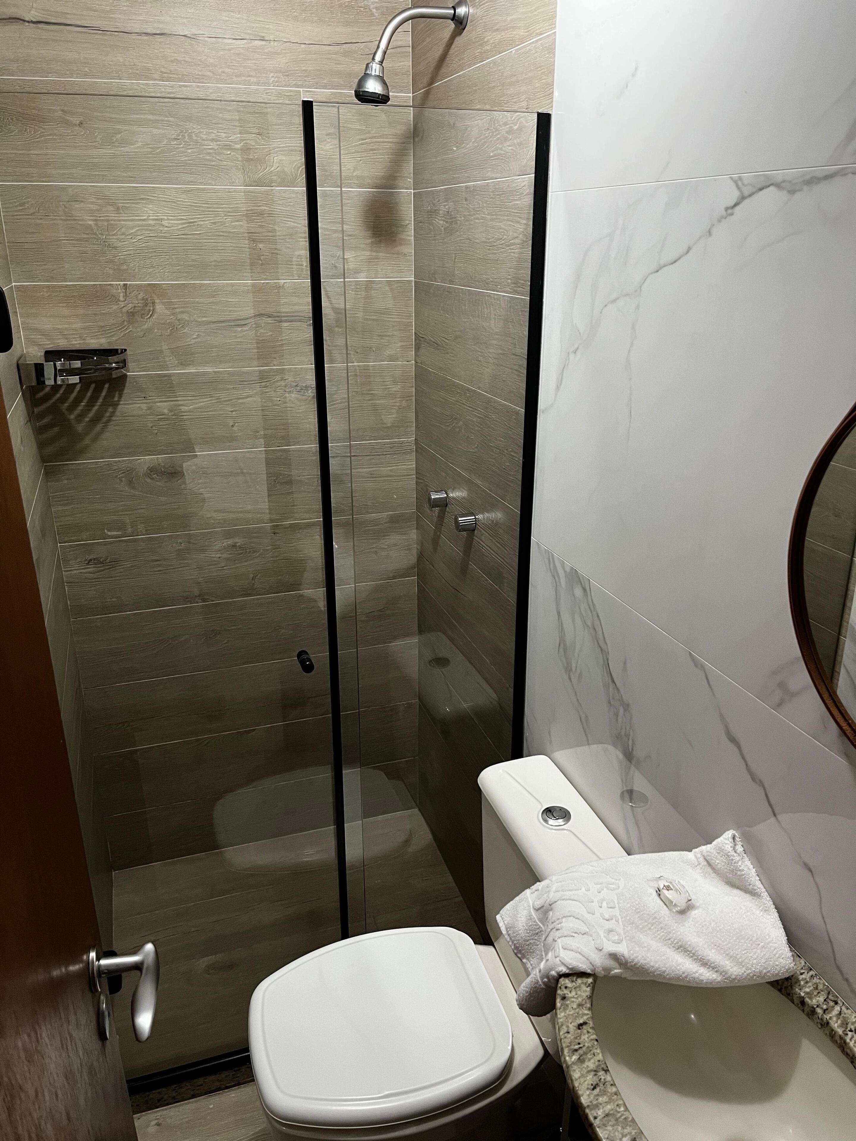 Een moderne badkamer met een douchecabine van glas, een wit toilet en een wand betegeld met marmer.