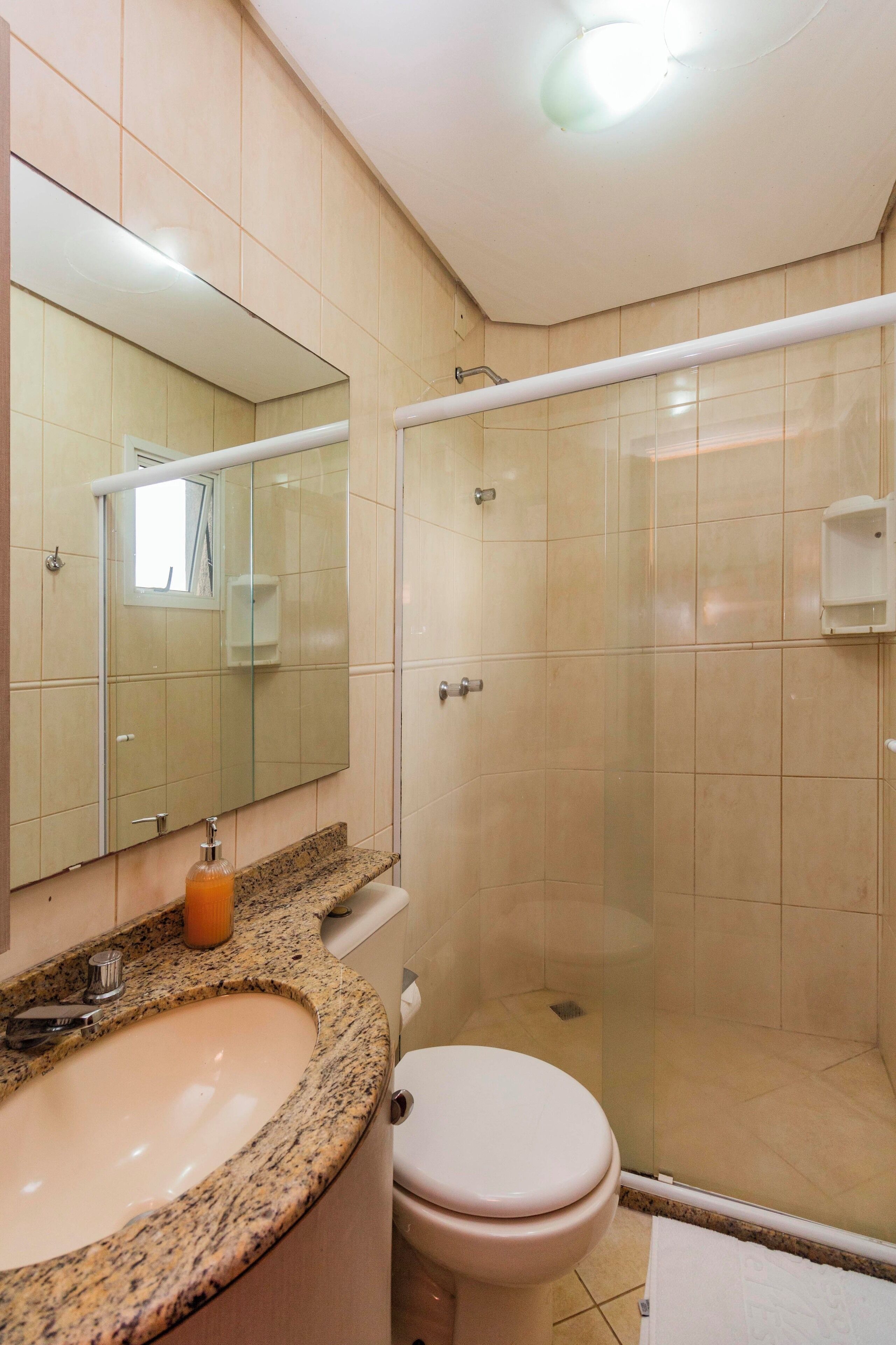 A bathroom with a granite countertop sink, a toilet, a glass shower enclosure, and a mirror.