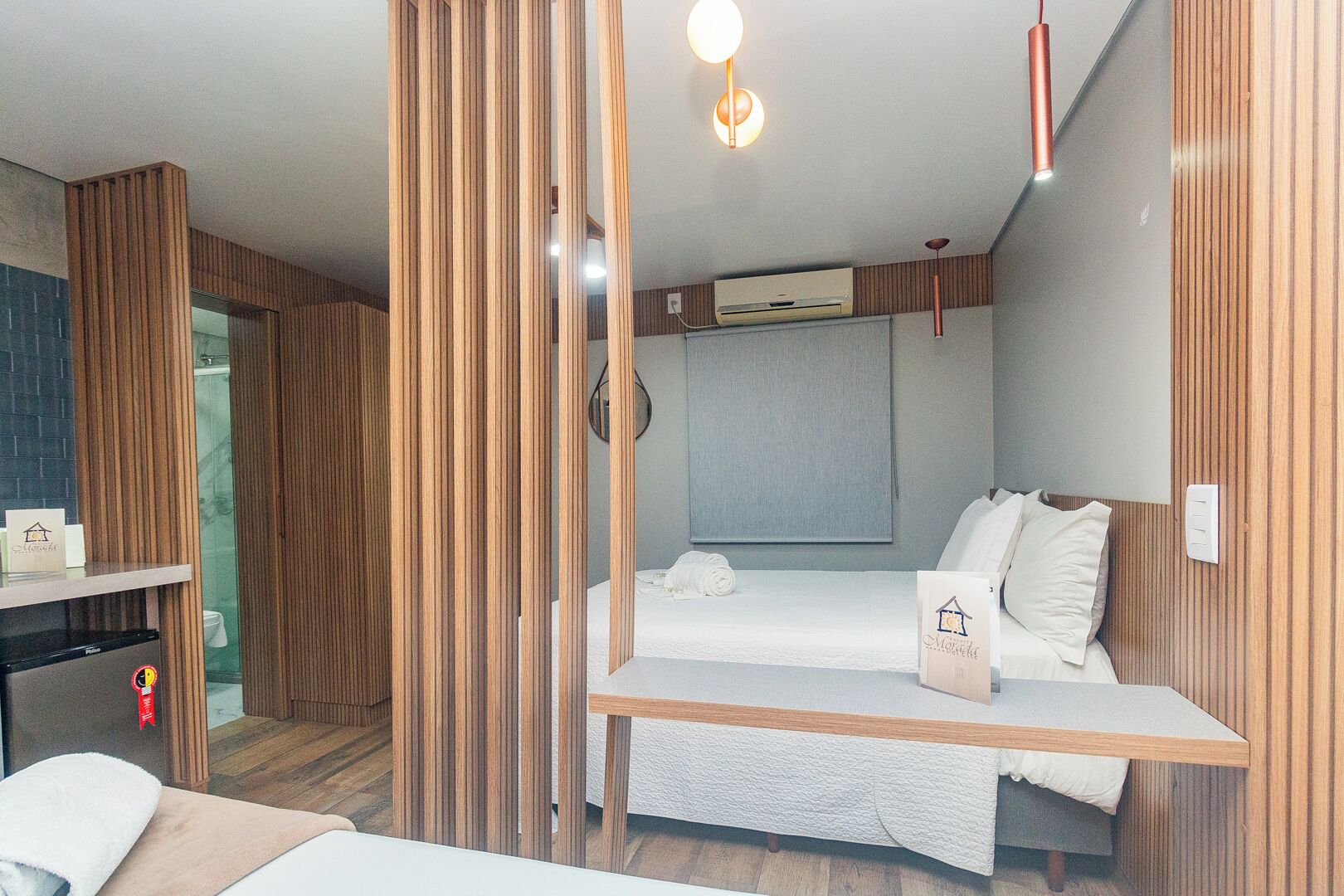 A modern hotel room with a bed, bedside table, and a small desk with a chair.