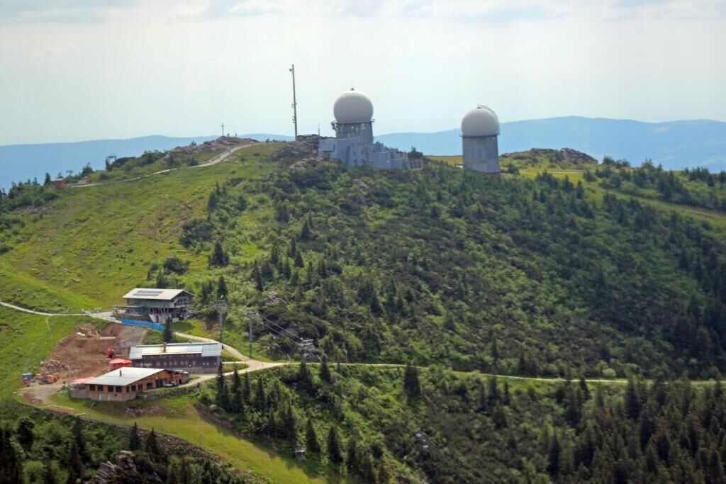 A mountainous area with a small building and two large spherical structures, likely observatories, on a hill.