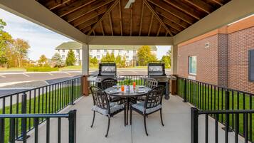 An outdoor patio with a brick wall, a covered area with a wooden ceiling, and a grill station.