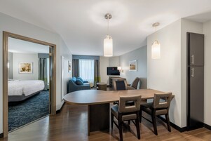 A hotel room with a dining area, a sofa, a TV, and a bed.
