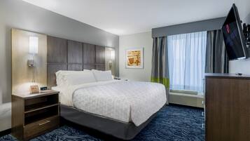 A hotel room with a bed, bedside table, lamp, artwork, and a TV on the wall.