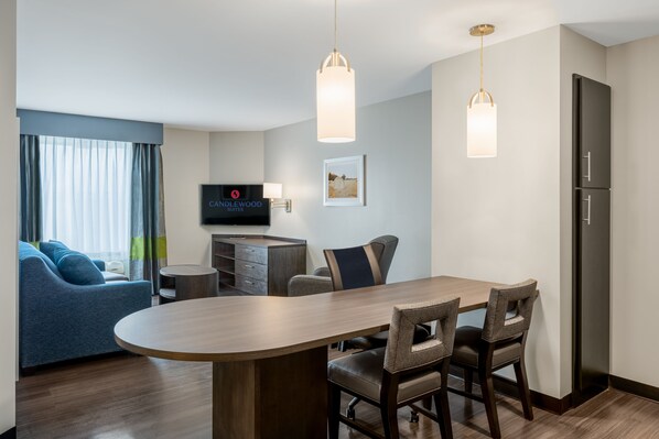 Una habitación de hotel moderna con zona de comedor, sofá, televisor y refrigerador.