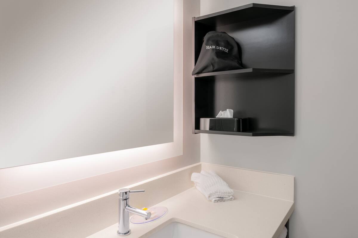 A bathroom with a white sink, a towel, and a hair dryer on a black shelf.
