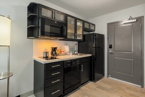 A modern kitchen with black cabinetry, a built-in microwave, a refrigerator, and a coffee maker. - Candlewood Suites Cookeville by IHG (Cookeville)