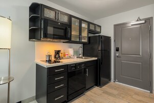 Una cocina moderna con armarios negros, microondas integrado, refrigerador y cafetera.