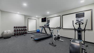 Un gimnasio con equipo de ejercicio, incluyendo una caminadora, bicicleta estática y pesas.