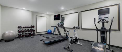 Un gimnasio con equipo de ejercicio, incluyendo una caminadora, bicicleta estática y pesas.