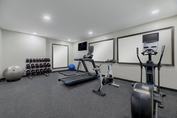 Un gimnasio con equipo de ejercicio, incluyendo una caminadora, bicicleta estática y pesas.