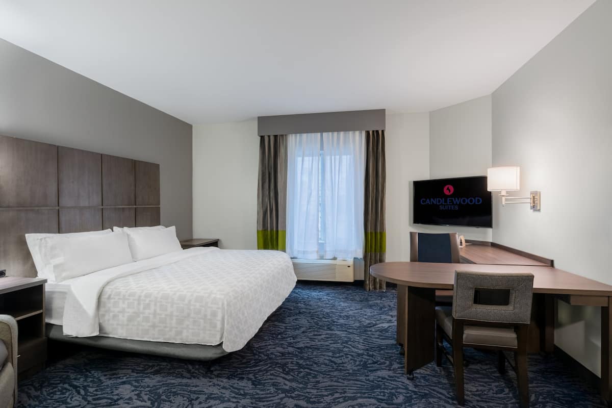A hotel room with a bed, a desk, a chair, a television, and a window with curtains.