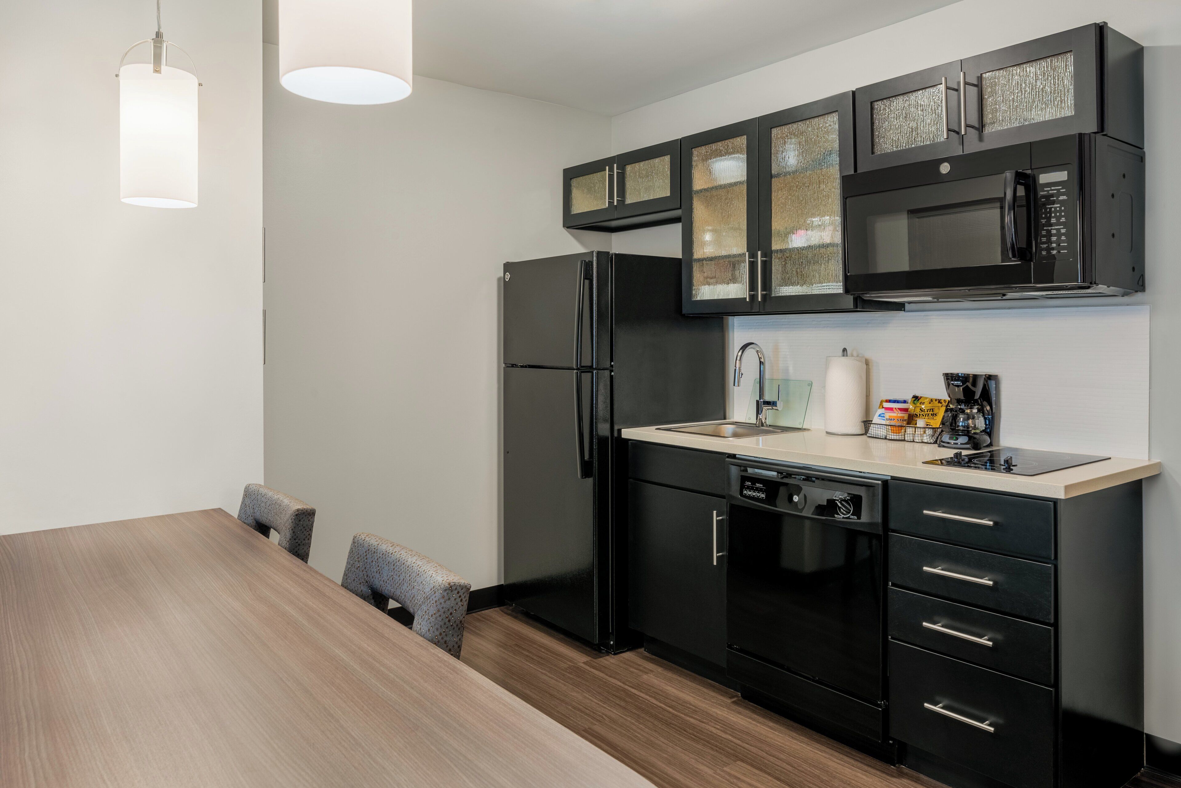 Une cuisine moderne avec des appareils électroménagers noirs, une table à manger en bois et un luminaire suspendu.