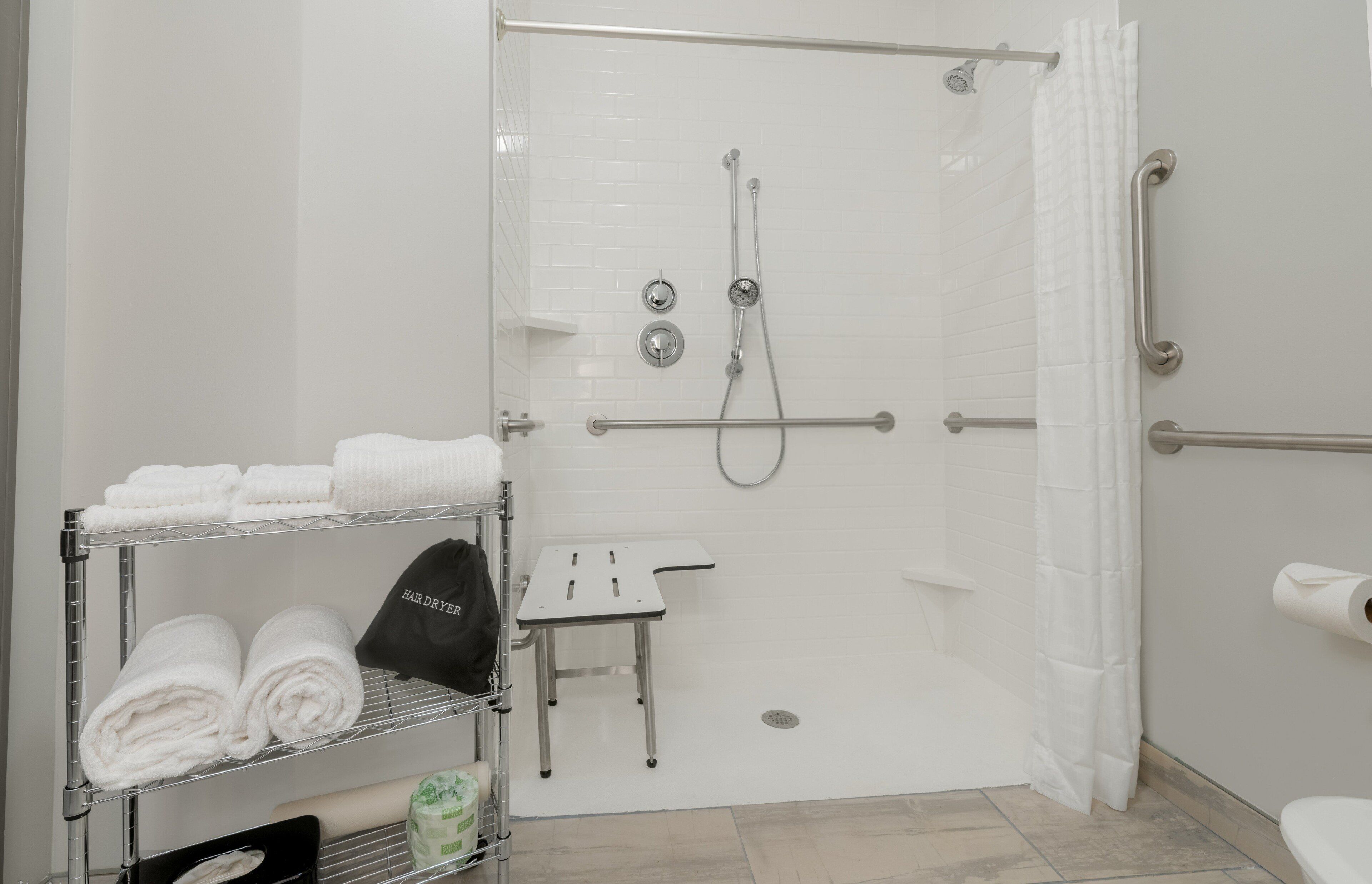 A modern bathroom with a walk-in shower, grab bars, a towel rack, and a small table.