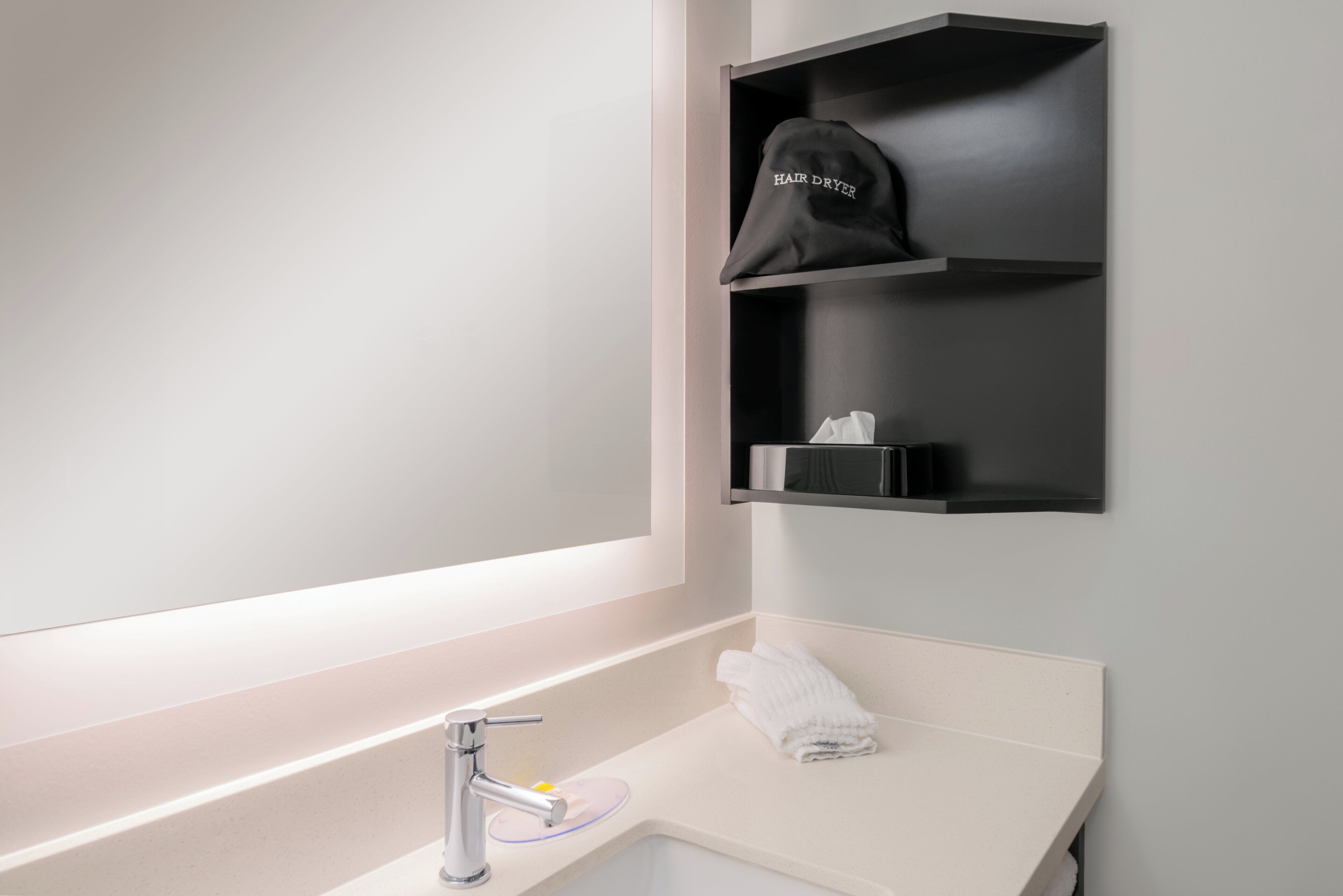 A bathroom with a mirror, a sink, a towel, and a hair dryer on a shelf.