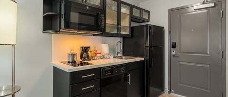 Una cocina moderna con armarios negros, un refrigerador de acero inoxidable y un microondas empotrado.