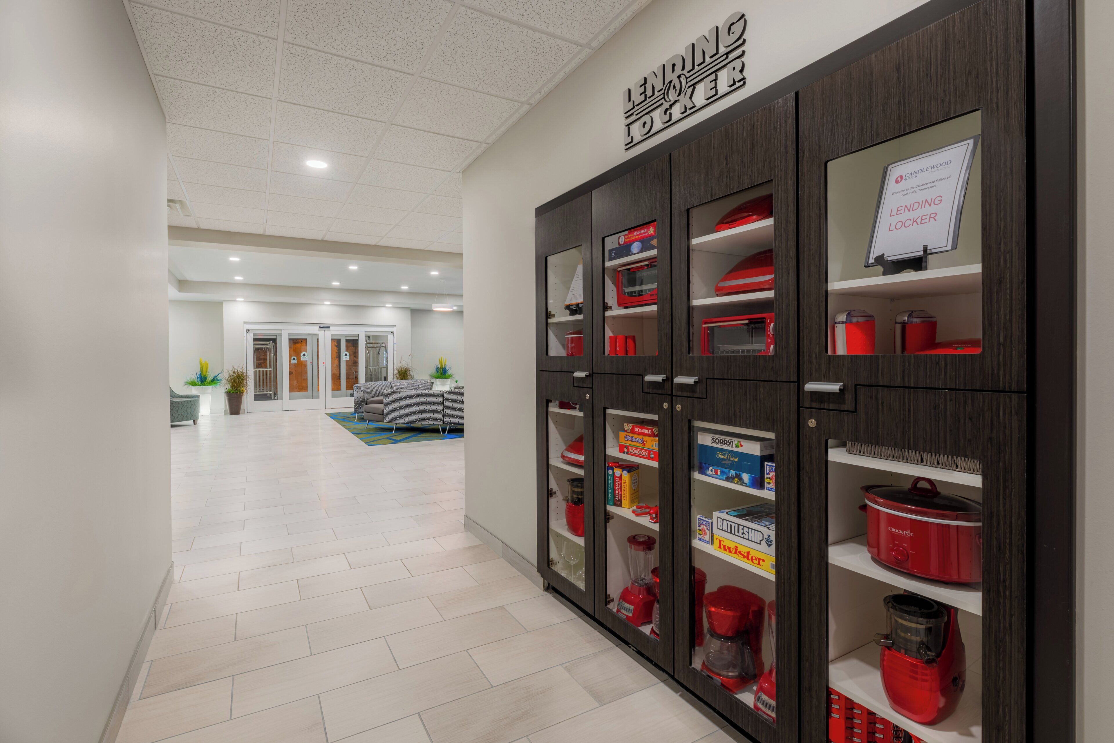 A hotel corridor with a modern design, featuring a central walkway and a row of lockers on the right.