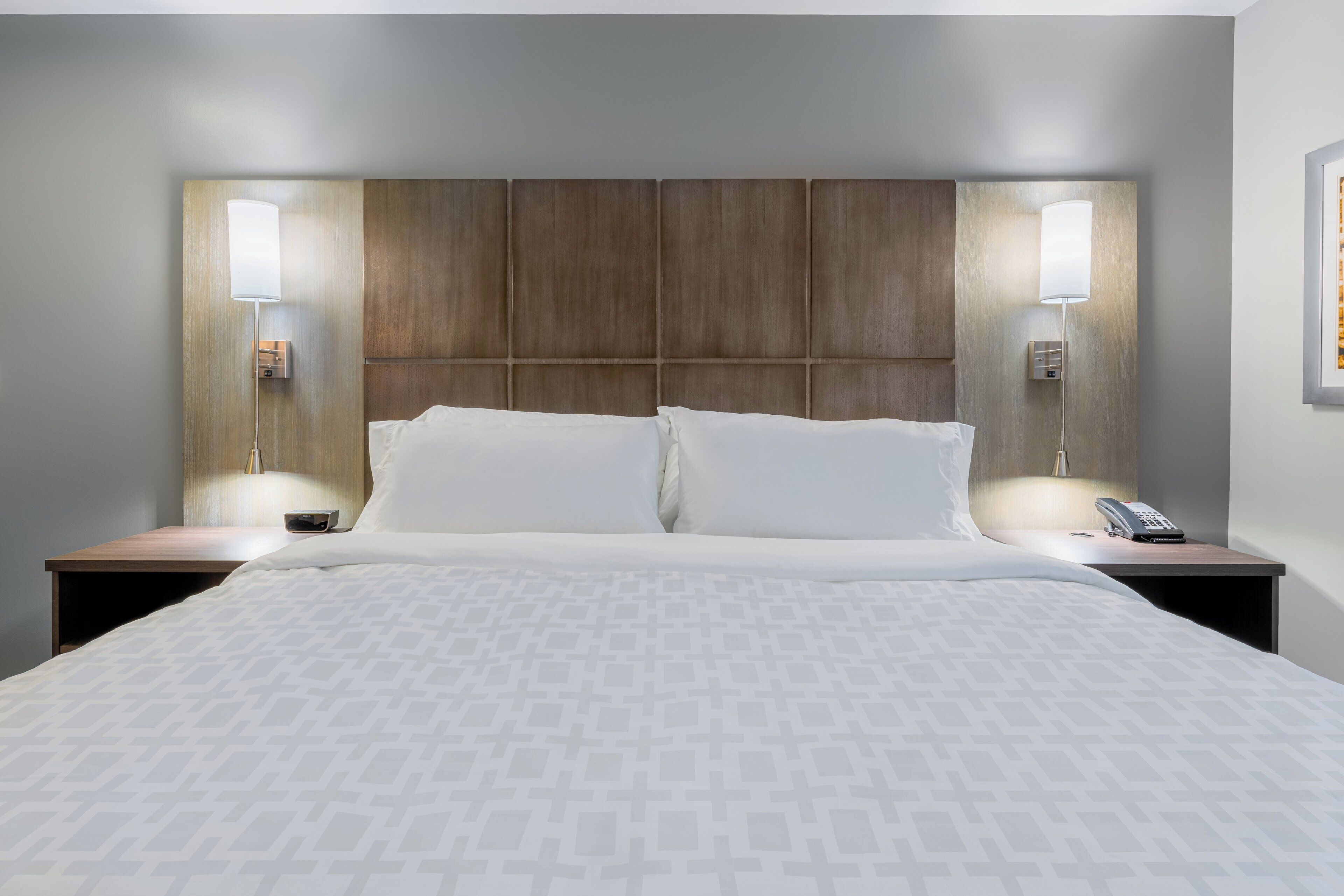 Une chambre d’hôtel avec un grand lit, deux tables de chevet, une tête de lit et deux lampes fixées au mur.