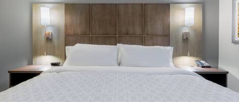 Una habitación de hotel con una cama grande, dos mesitas de noche, un cabecero y dos lámparas fijadas a la pared.