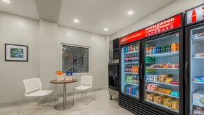 A modern refreshment area with two white chairs, a small table, and a refrigerator stocked with beverages and snacks. - Candlewood Suites Cookeville by IHG (Cookeville)