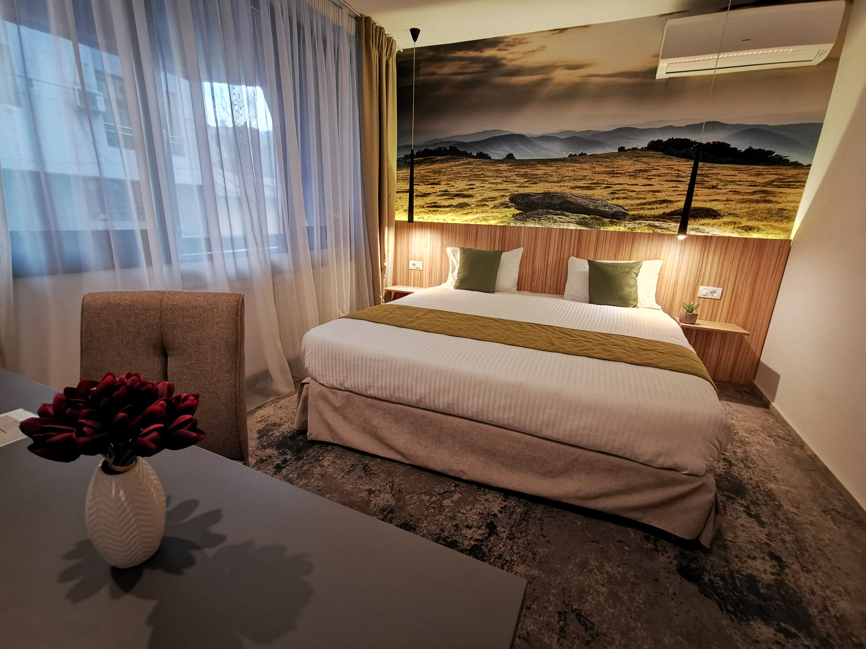 Una camera d'albergo con un letto, una sedia, un tavolo con un vaso e un condizionatore d'aria a parete.