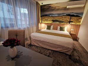 Una camera d'albergo con un letto, una sedia, un tavolo con un vaso e un condizionatore d'aria a parete.