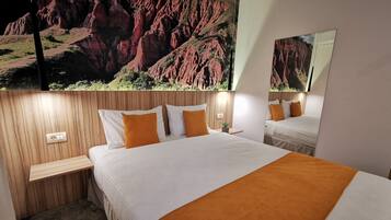 Habitación de hotel con una cama grande, dos mesitas de noche, un espejo y un mural en la pared que muestra un paisaje de rocas rojas.