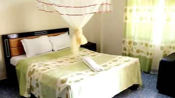 Un dormitorio con una cama, una mesita de noche, una silla, una mosquitera y una ventana con cortinas.