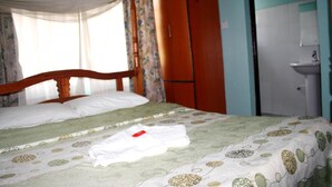 Quarto de hotel com cama, guarda-roupa, casa de banho com lavatório e janela com cortinas.