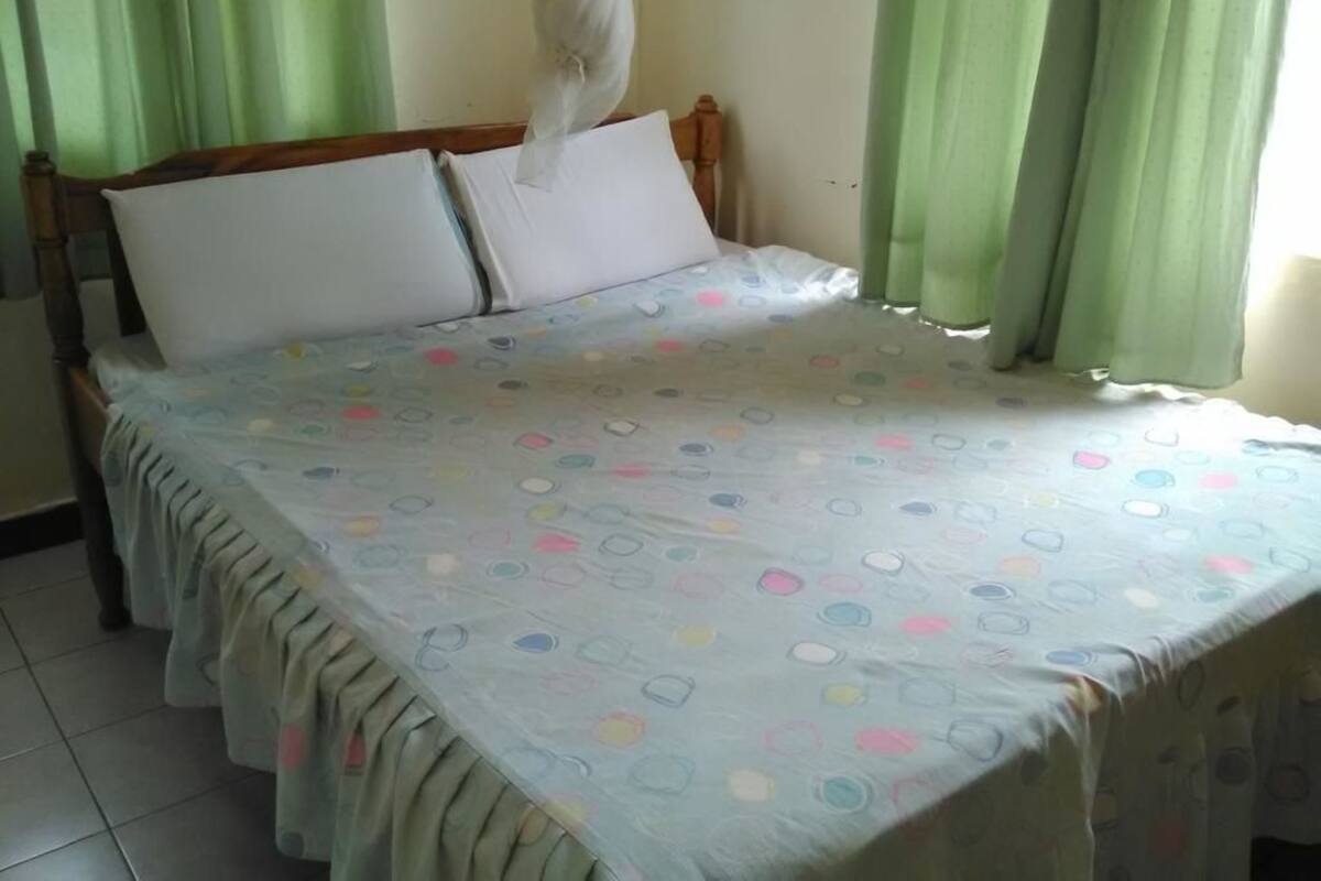 A bed with a patterned bedspread, a wooden headboard, and green curtains.