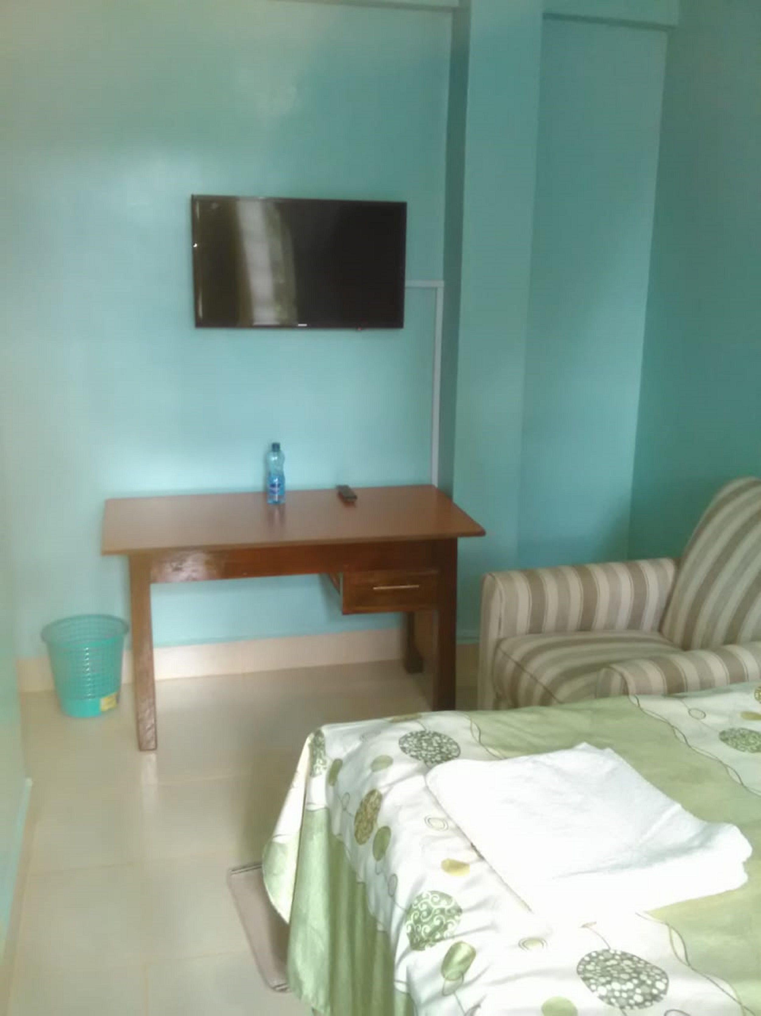 A room with a bed, a desk, a chair, a television, and a trash bin.
