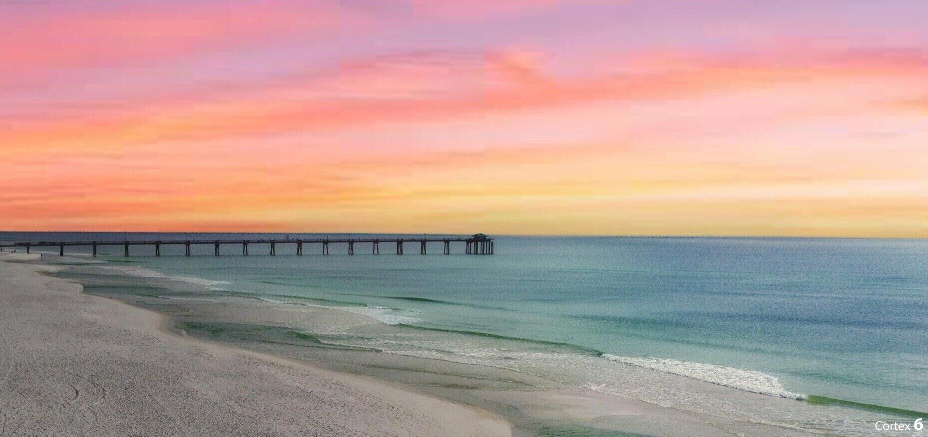 Une plage avec une jetée qui s’avance dans l’océan, un ciel dégagé et une eau calme.
