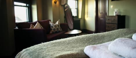A hotel room with a bed, a sofa, a small table, a dresser, and a TV on the wall.