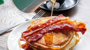 A plate of pancakes with bacon and syrup being poured from a mug. - Westow House - London Crystal Palace (London)