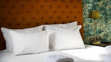 A neatly made bed with white linens and pillows, a tufted headboard, a lamp, and a floral wallpaper.
