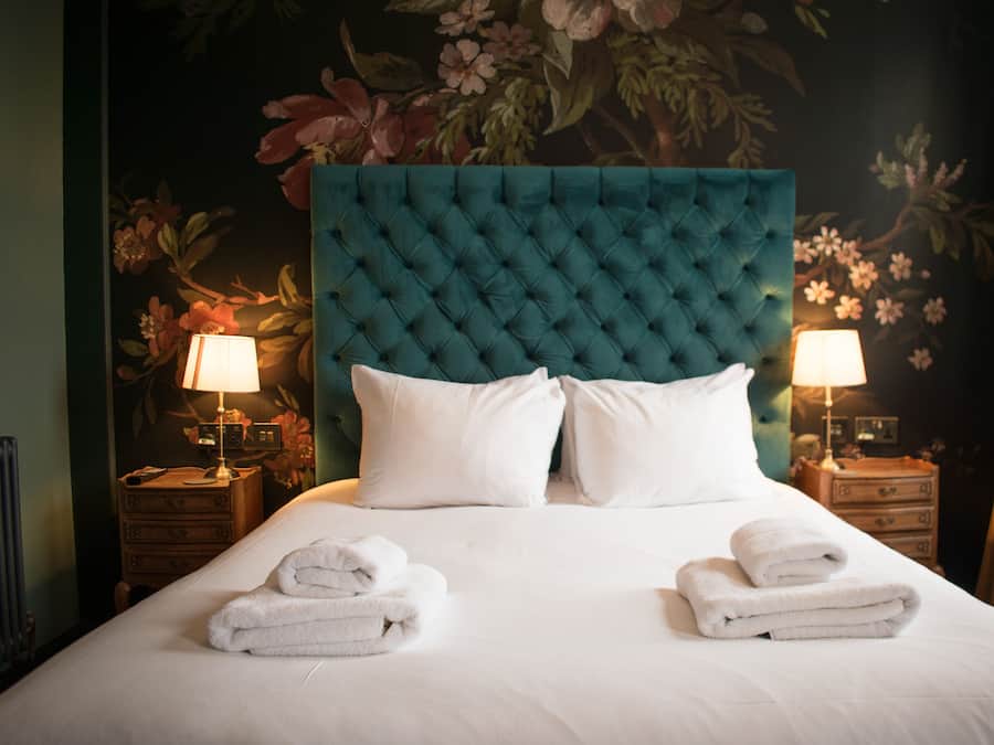 A neatly made bed with white linens and two towels folded at the foot.