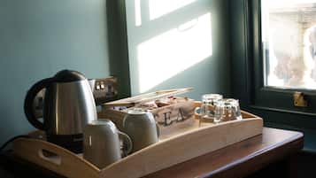 Un plateau en bois avec une bouilloire, des tasses et des verres, posé sur une table près d’une fenêtre.